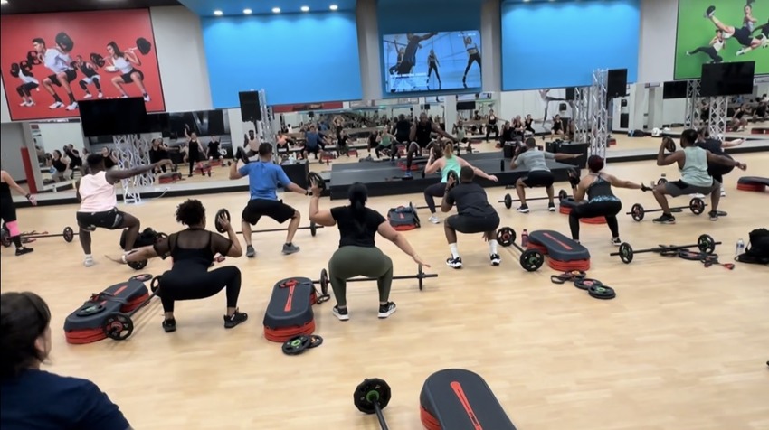 CLUB4 instructor guiding participants through a dynamic workout in a bright studio.