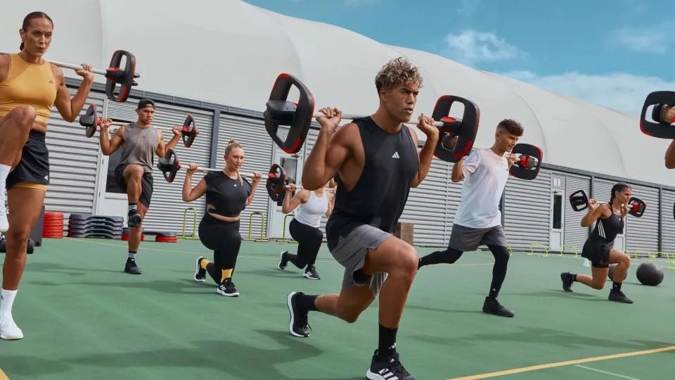 Ben Main lunges with a barbell leading a group of people in an outdoor BODYPUMP workout.