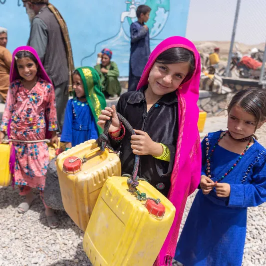 Four children in colorful clothing fetch water using water jugs