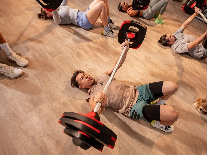 Close-up of two people lifting heavy barbells during a strength training class, showcasing effort and community support.